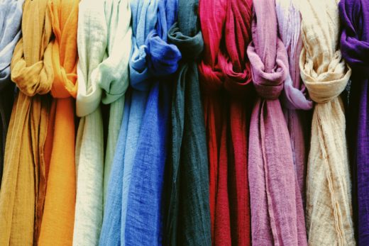 Scarves of various bright colours knotted around a rail, hanging in a row