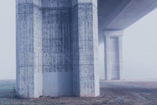 Grey concrete support pillars under a bridge, in grey mist.