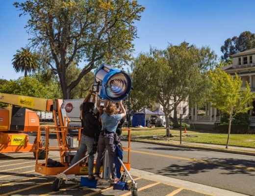 Image of a lighting crew rigging a large HMI on a stand.