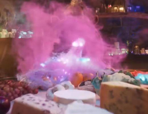 The BFG character looks over a table as it is filled with food by a purplish cloud of magical dust.